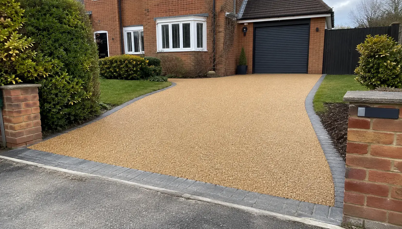 New buff gold resin bound driveway with grey block paving edging outside a detached brick house in Cambridgeshire.