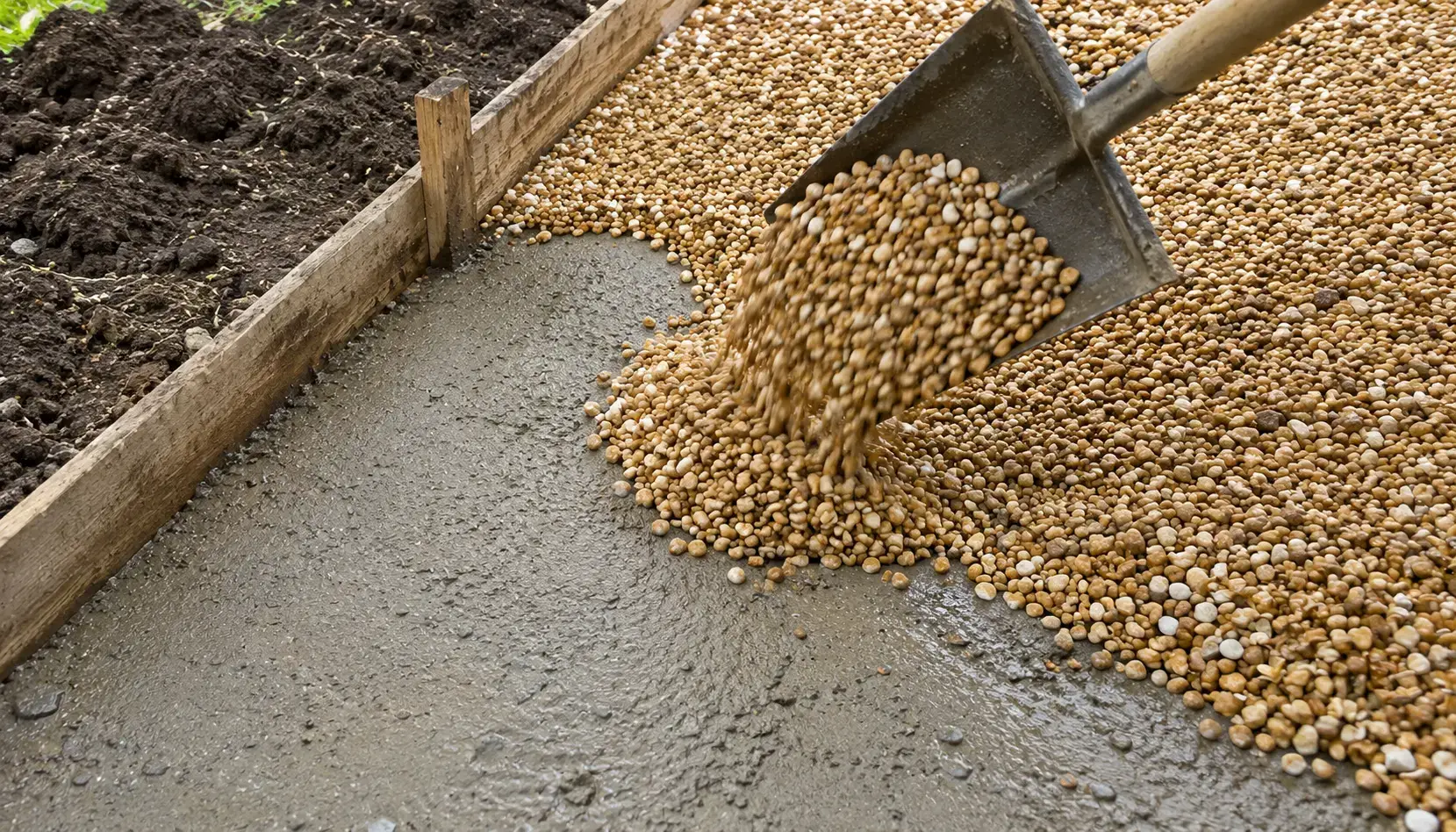 Close-up of golden buff pea shingle gravel being shovelled onto a damp compacted sub-base over fenland clay during a gravel driveway installation in Cambridgeshire.