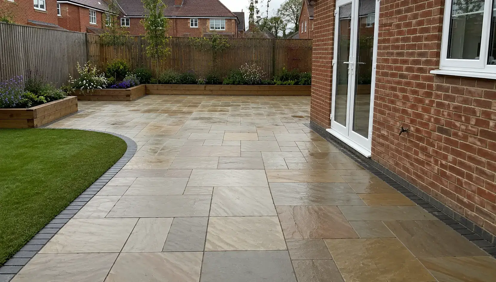 Large Indian sandstone patio with landscaped lawn, raised flower beds and brick house garden in Ely, Cambridgeshire.